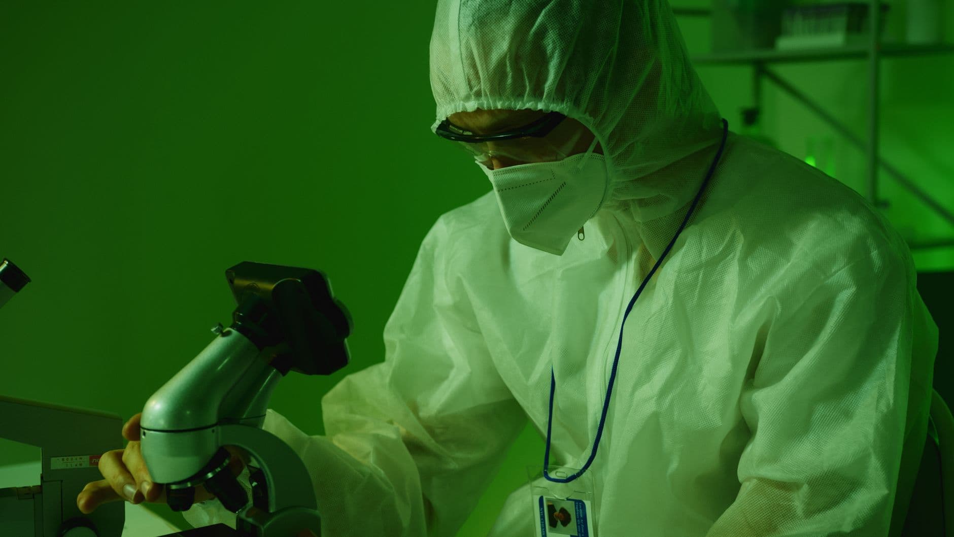 Medical professional in protective gear using a microscope in a laboratory setting.