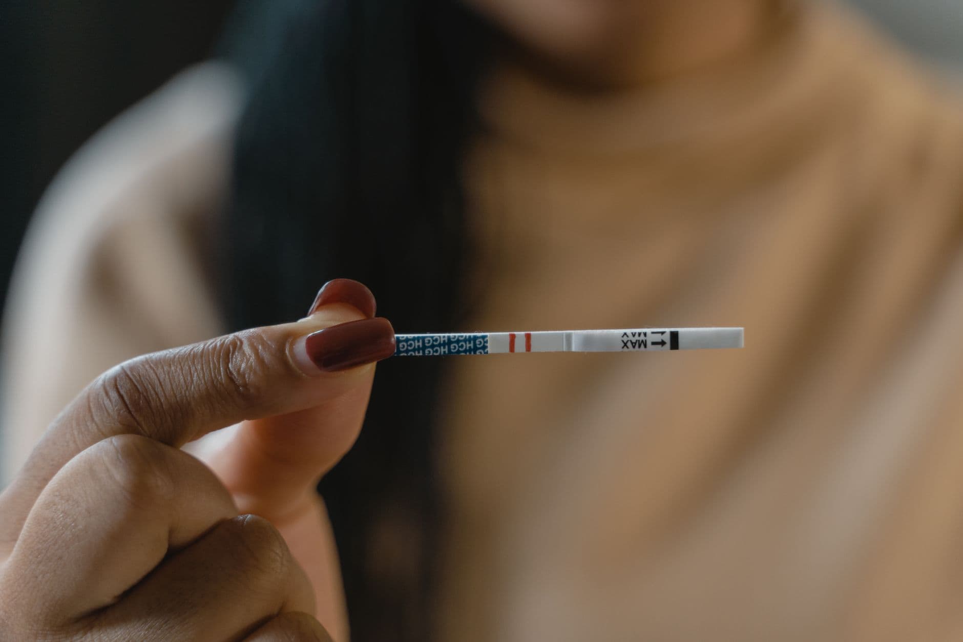 A hand holds a positive pregnancy test strip against a blurred background, symbolizing new beginnings.