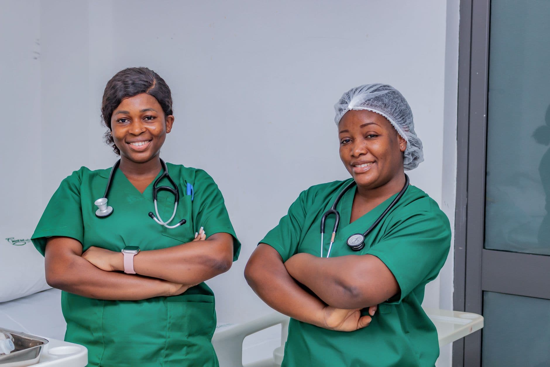 Two nursing students in green scrubs smiling confidently in a clinical training setting.